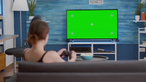 Νεαρή γυναίκα κρατώντας ασύρματο χειριστήριο παίζει παιχνίδι δράσης κονσόλα βίντεο στην πράσινη τηλεόραση - Πλάνα, βίντεο