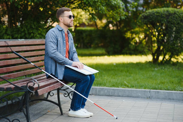 Blind man reading book on bench in park. - Foto, imagen