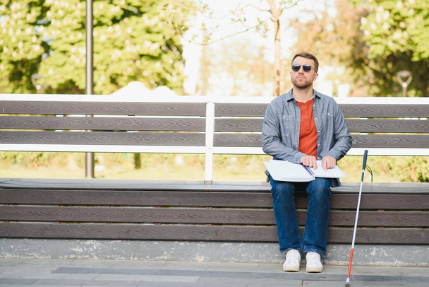 Visually impaired man with walking stick, sitting on bench in city park. Copy space. - Foto, immagini