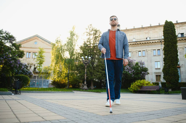 Молодой красивый слепой мужчина ходит с палкой в городе. - Фото, изображение
