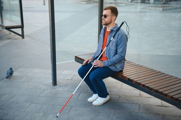Visually impaired man with walking stick, sitting on bench in city park. Copy space. - Fotoğraf, Görsel