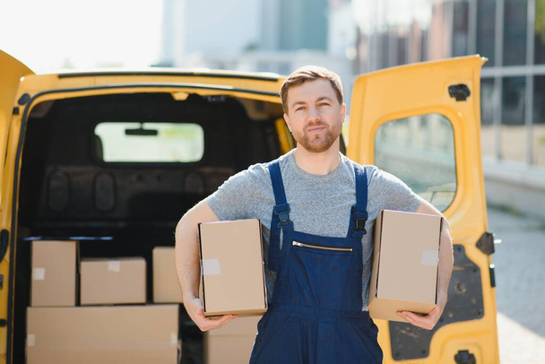 delivery service employee. Portrait of man working in delivery service. Portrait of courier with box. Courier next to minivan. Delivery service career - Fotó, kép