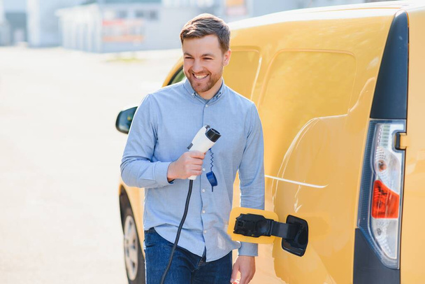 Smiling man unplugging the charger from the car. - Foto, Imagen