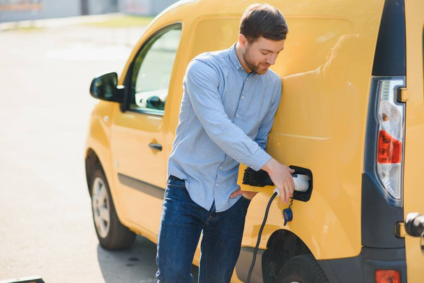 Smiling man unplugging the charger from the car. - 写真・画像