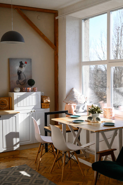 Κάθετη φωτογραφία της κουζίνας σε μοντέρνο στυλ με ξύλινα στοιχεία, λευκές προσόψεις, παρκέ δάπεδο. Ένα μεγάλο παράθυρο στην κουζίνα. - Φωτογραφία, εικόνα