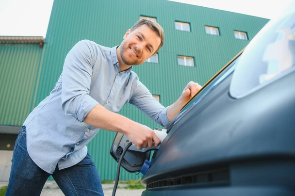 Smiling man unplugging the charger from the car. - Foto, Imagem