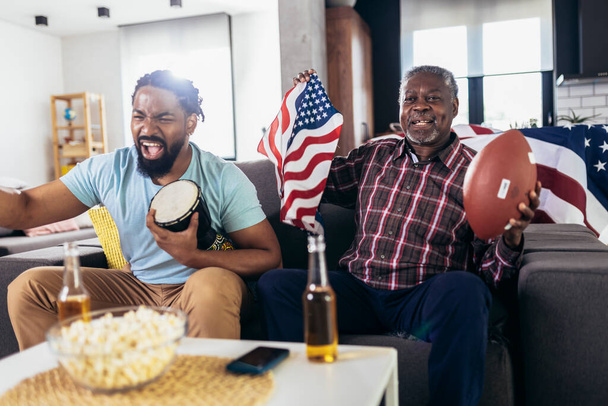 Senior father and adult son cheering for american football game at home - Fotoğraf, Görsel