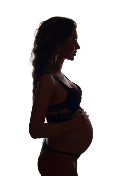 Una mujer embarazada blanca joven está embarazada de nueve meses con un fondo brillante. Preparación para la maternidad - Foto, Imagen