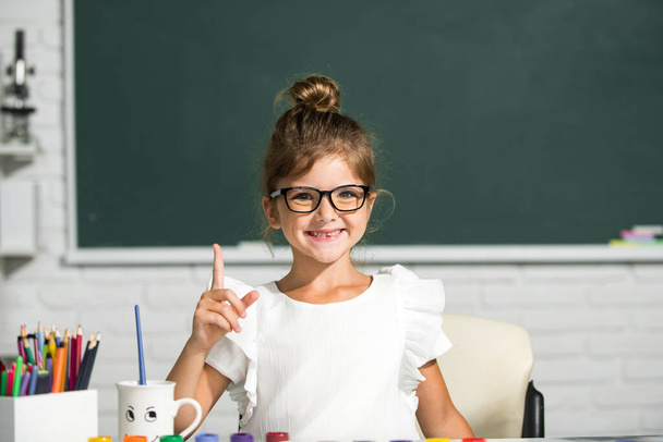 Cute little girl child painting with paints color and brush. Drawing lesson in school. Funny school girl face with glasses. - Φωτογραφία, εικόνα