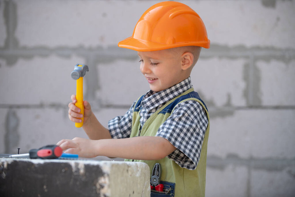 Little boy in orange protective helmet with instruments for renovation. Repair home. - Photo, Image
