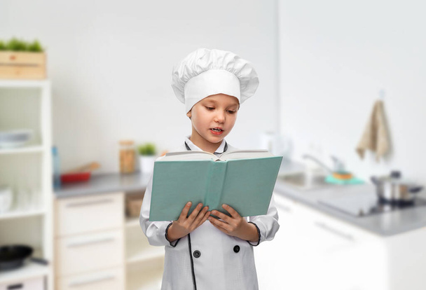 girl in chefs toque reading cook book in kitchen - 写真・画像