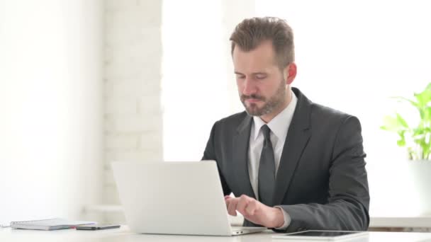 Молодий бізнесмен посміхається в камері, користуючись ноутбуком у офісі - Кадри, відео