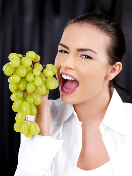 Young woman about to bite into a bunch of grapes - Фото, зображення