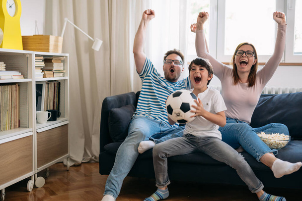 one child family cheering and watching soccer game at home - Φωτογραφία, εικόνα