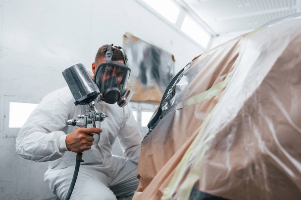 Painting job in progress. Caucasian automobile repairman in uniform works in garage. - Foto, Bild
