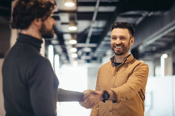 Důvěryhodní šťastní podnikatelé si potřásají rukou, aby uzavřeli dohodu nebo dohodu v moderní kancelářské budově - Fotografie, Obrázek
