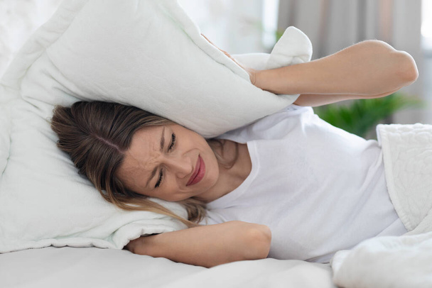 Furioso sem sono jovem mulher cobrindo a cabeça com travesseiro - Foto, Imagem