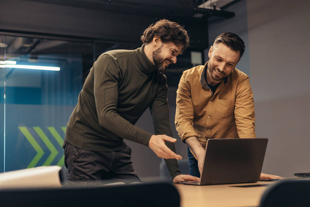 Employés masculins positifs discutant du projet d'entreprise, utilisant l'ordinateur portable, remue-méninges pour des idées au bureau de l'entreprise - Photo, image
