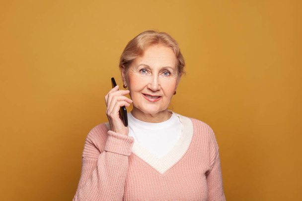 Ευτυχισμένη ηλικιωμένη γυναίκα με smartphone σε φωτεινό κίτρινο φόντο close up πορτρέτο - Φωτογραφία, εικόνα