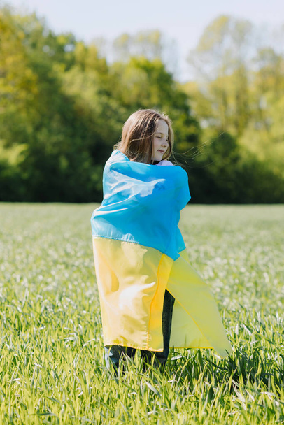 Happy smiling Ukrainian girl in an embroidered shirt with a yellow and blue flag in a field on a background of forest. Independence Day of Ukraine. Day of the State Flag of Ukraine. High quality photo - Photo, Image