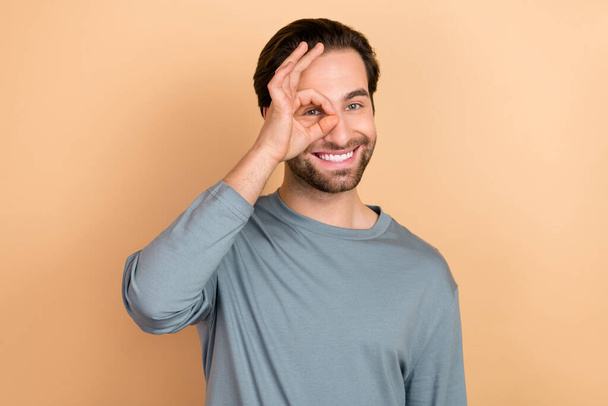 Photo of cheerful friendly person hand fingers make okey symbol eye look camera isolated on beige color background - Photo, image