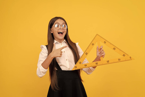 niño sorprendido en uniforme escolar y gafas sostienen triángulo matemático para medir, trigonometría - Foto, Imagen