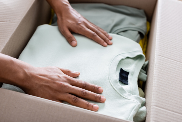 Cropped view of african american seller putting clothes in package in online web store  - 写真・画像
