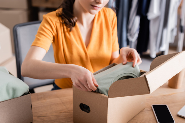 Cropped view of owner putting clothes in box in online web store  - Foto, afbeelding
