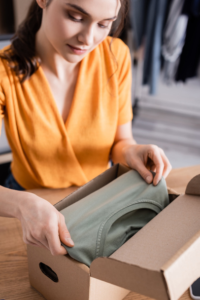 Young seller putting clothes in package in online web store  - 写真・画像