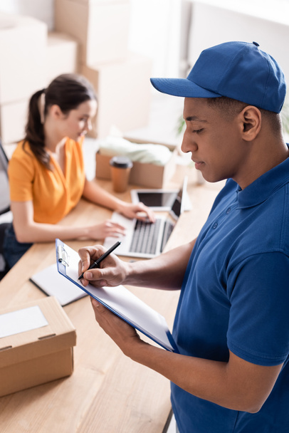 African american deliveryman writing on clipboard in online web store  - 写真・画像