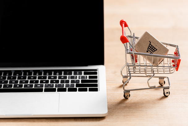 Toy shopping cart with package near laptop with blank screen on table  - Photo, Image