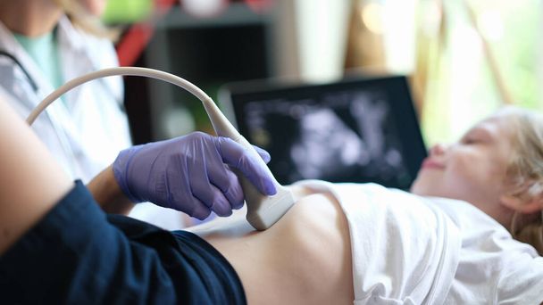 Doctor make ultrasound of abdominal cavity for girl using scanner in clinic - Photo, Image
