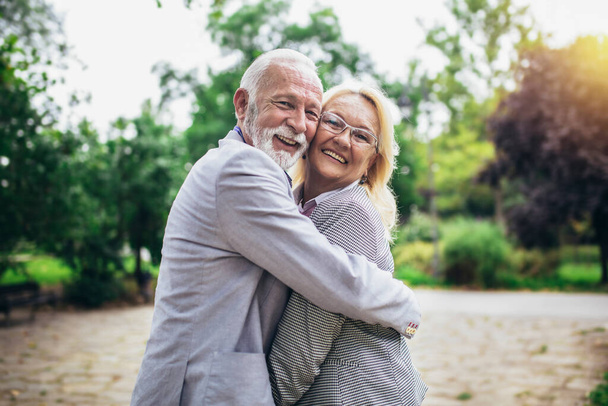 Senior active caucasian couple hugging looks happy in the park in the afternoon - Photo, Image
