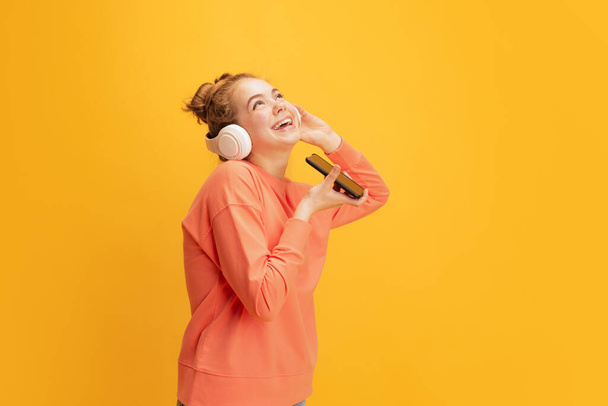 Portrét mladé roztomilé dívky, student nahrávání hlasové zprávy s telefonem, pózování v ležérní látky izolované přes žluté pozadí - Fotografie, Obrázek