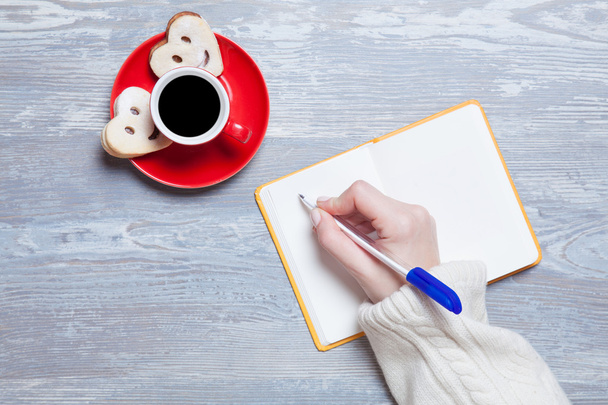 Frau schreibt etwas in Notizbuch neben Tasse Kaffee. - Foto, Bild