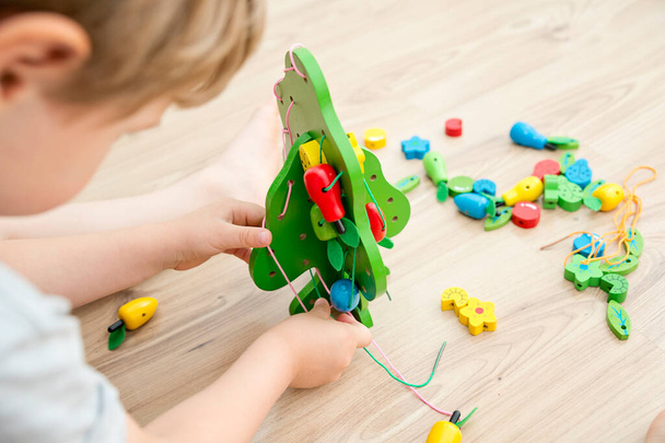 Fine-motoric skils. Stringing Beads Toys for infants and toddlers. Threading Activity for Children. boy sitting on the floor and plays with wooden tree and garden goods. - Фото, зображення