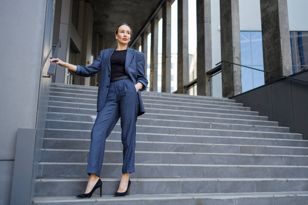 Стильно одетая женщина позирует на лестнице современного здания - Фото, изображение