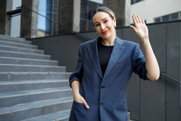 Donna d'affari agitando mano stand sullo sfondo di un edificio moderno - Foto, immagini
