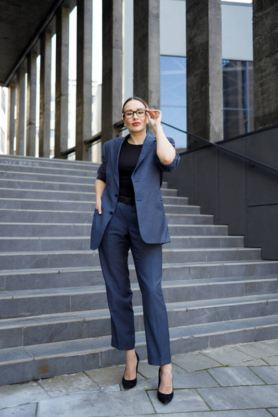 Κομψή γυναίκα επιχειρηματίας σε γυαλιά στέκεται έξω από ένα σύγχρονο κτίριο γραφείων - Φωτογραφία, εικόνα