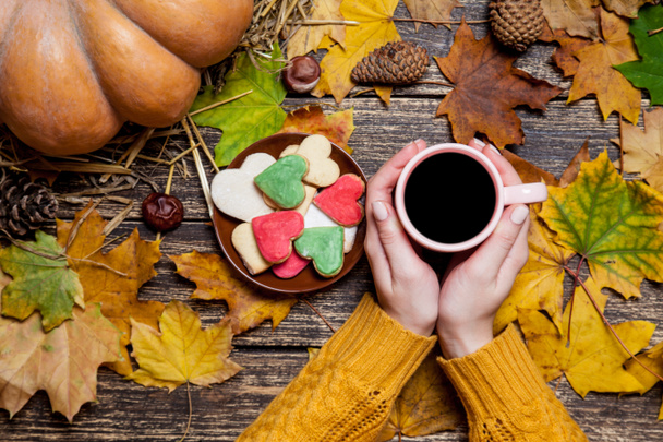 Femme tenant une tasse de café près de cookies sur fond d'automne
. - Photo, image
