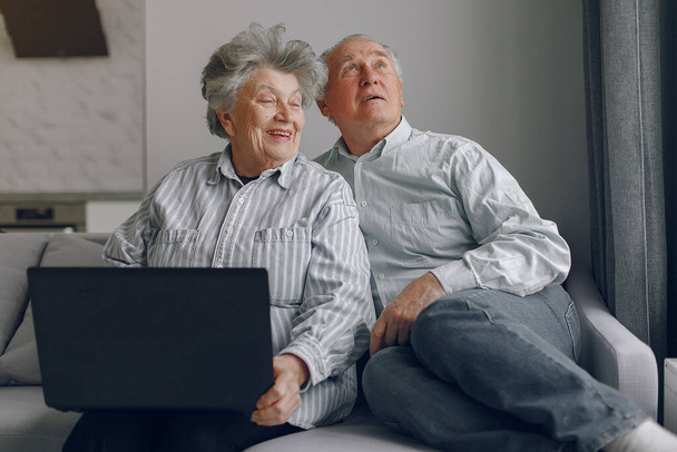 Elegante oude paar zitten thuis en met behulp van een laptop - Foto, afbeelding