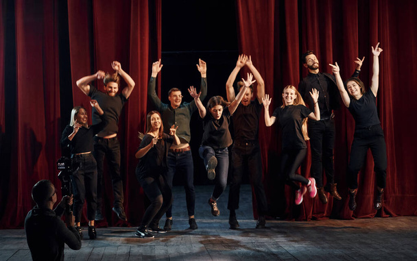 Happy people celebrating success. Group of actors in dark colored clothes on rehearsal in the theater. - Фото, зображення