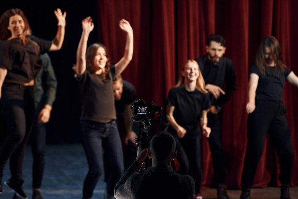 Happy people celebrating success. Group of actors in dark colored clothes on rehearsal in the theater. - Foto, afbeelding