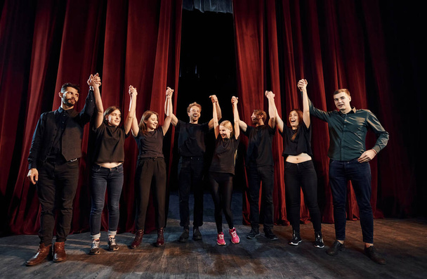 People bowing to audience. Group of actors in dark colored clothes on rehearsal in the theater. - Foto, afbeelding