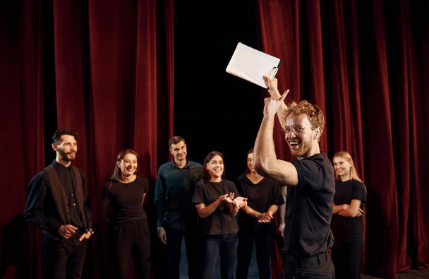Man with notepad practice his role. Group of actors in dark colored clothes on rehearsal in the theater. - Foto, immagini