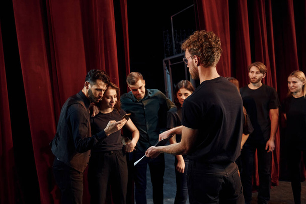 Man with notepad practice his role. Group of actors in dark colored clothes on rehearsal in the theater. - Foto, Bild