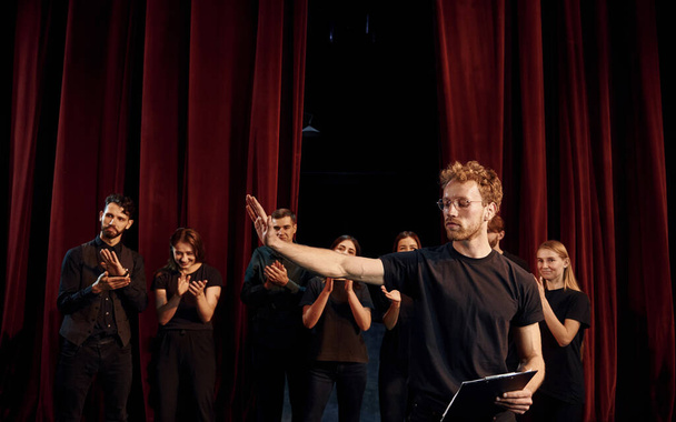 Man with notepad practice his role. Group of actors in dark colored clothes on rehearsal in the theater. - Foto, Imagem