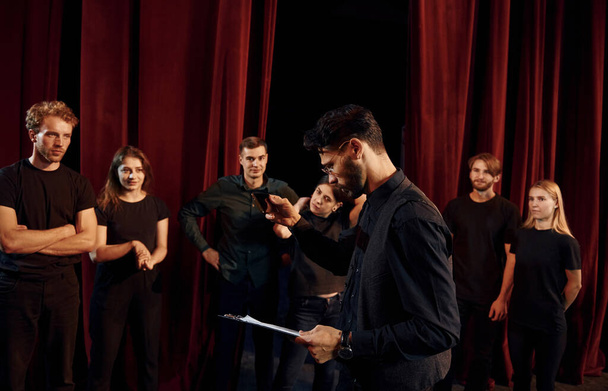 Expressionalible guy practicing his role. Group of actors in dark colored clothes on rehearsal in the theater. - Photo, image