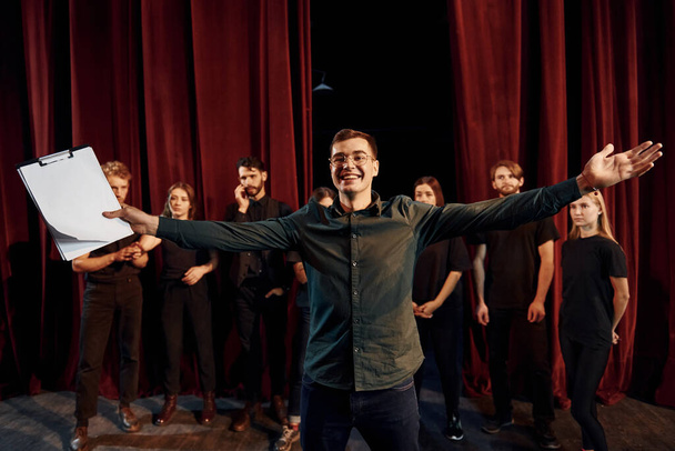 Man is practicing his role. Group of actors in dark colored clothes on rehearsal in the theater. - Foto, afbeelding