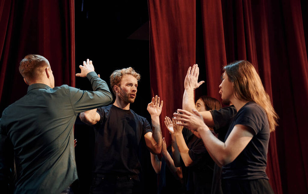 Giving high five, celebrating success. Group of actors in dark colored clothes on rehearsal in the theater. - Foto, Imagem